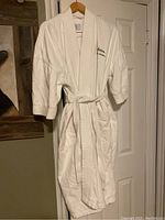 Front view of white Radisson hotel cotton robe hanging on wall, showing embroidered logo and belt tied at waist.