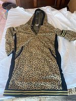 Full view of cheetah print hoodie dress with black side panels and striped ribbed cuffs laid flat on a white surface.