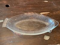 Top angled view of clear fish-shaped glass platter showing textured scales and fin detail, including flea chip on fin.