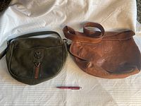 Photo of both purses side by side with a pen for scale on a white surface. Khaki purse on left, camel purse on right.
