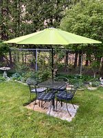 Full view of metal mesh black bistro table with four attached chairs and lime green umbrella open outdoors.