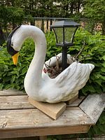 Concrete swan garden ornament on wooden bench with a black solar garden light and visible soil inside the cavity.