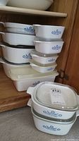Full set of ten Corning Ware blue cornflower casseroles in cabinet showing varying sizes and lids