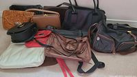 Photo showing a variety of handbags in multiple colors and styles including hand-tooled leather, shoulder and crossbody bags.