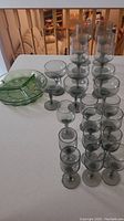 Full set of smokey grey stemware pieces arranged near green glass divided dish on a white surface.
