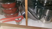Photo showing three red Gorica pots with lids stacked, orange-handled potato ricer, and stainless steel kitchen containers.
