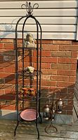 Full view of black metal rack with four shelves, displaying concrete frogs, mini planters, pink saucer and brass candle holder nearby.