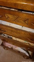 Photo of a vintage wooden dresser drawer partially opened showing stacked table linens including embroidered fabric with floral designs.