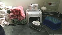 Entire lot displayed on floor including stacked towels, vanity set, stools, pumice stone and bath sponge, and hanging shower caddy.