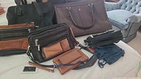 Lot with two Ashlin cross body bags with built-in wallets, a brown leather wrist clutch, and a large Targus travel bag on a bed.