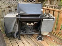 Overall view of grill on open cart with propane tank, side shelves, cover