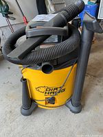 Photo of Dirt Hawg vacuum showing yellow body, brand logo, and attached hose and attachments.