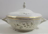 Side view of porcelain serving bowl with blossom pattern and lid, showing gold trim and handles.
