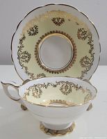 Photo showing the tea cup positioned in front of the saucer, highlighting the pale yellow color and detailed gold gilded pattern on both.