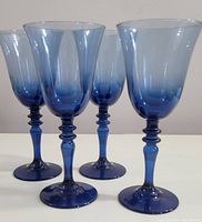 Photo showing four midnight blue ombre blown glass goblets standing upright, highlighting their gradient color and detailed stems.