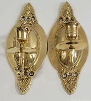 Front view of two solid brass wall sconce candlestick holders showing design details and condition.
