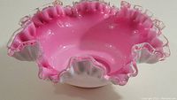 Front and angled views showing the pink interior and white exterior with ruffled clear glass edge of the berry bowl.