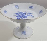 Side angled view of the white porcelain floral compote with blue floral patterns and gold trim on rim and pedestal base.