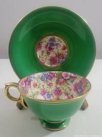 Front angled view of green tea cup and saucer showing floral interior and gold accents