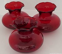 Front view of three vintage ruby glass vases with scalloped rims showing deep red translucent glass and rounded shape.