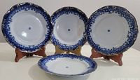 Four vintage Apulum porcelain side plates arranged upright on wooden plate stands, showing the ornate flow blue design with silver trim on the edges.