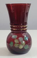 Full front view of the ruby glass vase showing overall shape, enamel floral decoration, and gold bands on the neck.