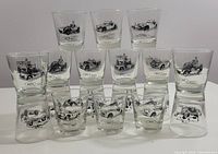 Front view of all 18 vintage Dominion Glass whiskey glasses arranged with various antique car designs printed on each glass.