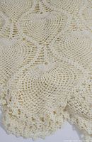Close-up image showing the detailed crochet pattern and scalloped lace edge of the pale yellow round tablecloth.