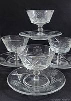 Four vintage etched pinwheel crystal dessert cups on stems with matching saucers arranged on black background.