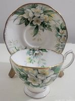 Photo showing the tea cup and saucer set with floral orange blossom design and gold trim, cup in front of saucer