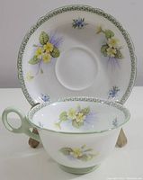 Shelley cup and saucer set displayed on a stand showing front view with floral designs and green scroll border.