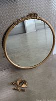 Full view of the large round mirror showing the gold painted wood frame with broken decorative top pieces separated on the floor.