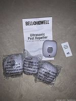 Bell Howell Ultrasonic Pest Repeller device, instruction manual, and two sealed plastic packages on concrete floor.