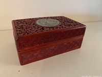Carved wooden box displaying floral motifs and central pearlized circular inlay on lid, angled view showing side and top pattern detail.