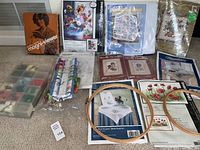 Full view of all included items arranged on carpet: kits, floss box, wooden hoops, magnifier viewer in original box, and various patterns.