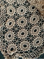 Close-up of beige crocheted tablecloth pattern showing circular and floral openwork design.