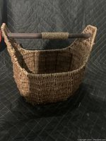 Front angle photo showing woven basket construction and wooden handle wrapped with rope at center