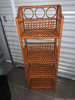 Front view showing the full four shelves and woven rattan construction with circular decorative elements on top.