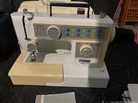 Front and side view of NELCO Ultra 5102A sewing machine with stitch pattern display and control dials. Beige and off-white casing with handle on top and spool of thread.