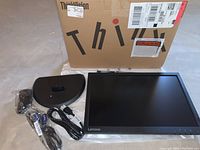 Photo showing Lenovo ThinkVision LCD monitor with stand base and cables in front of original box.