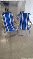 Two retro lawn chairs side by side showing full view of striped fabric and metal frame.