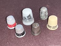All six thimbles arranged in a group on purple surface showing different materials, colors and labels.
