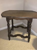 Side view of vintage solid wood side table showing turned legs and curved stretcher bars.
