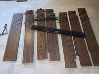 Photo showing twelve 48-inch by 8-inch wood shelf boards, one 48-inch by 1-inch narrow board, stacked with four long black metal racks, and a few wooden mounting brackets coiled with metal bands.