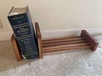 Side view of wooden bookshelf with Jane Austen complete novels boxed set placed standing upright on the left end of the shelf. Shelf has slatted wooden base and vertical side supports, medium brown color.