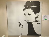 Front view of large square black and white Audrey Hepburn canvas print lying against a wall. Shows the minimalist style image.