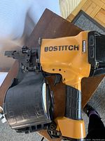 Left-side view showing yellow magnesium body, black grip, coil magazine and nail feed assembly