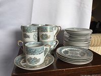 Display of mugs stacked with accompanying saucers and plates showing floral bone china design with gold accents.