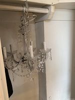 Vintage crystal chandelier hanging by chain with 5 electric candle-style arms decorated with hanging glass prisms and beads, photographed from side angle.