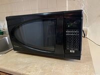 Left-front angled view of a black Danby microwave oven on a countertop, showing the keypad, display, and door with handle.